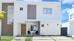 Une maison moderne à deux étages, dotée d’un toit plat, d’un petit patio avec une table et des chaises, et d’une pelouse bien entretenue.