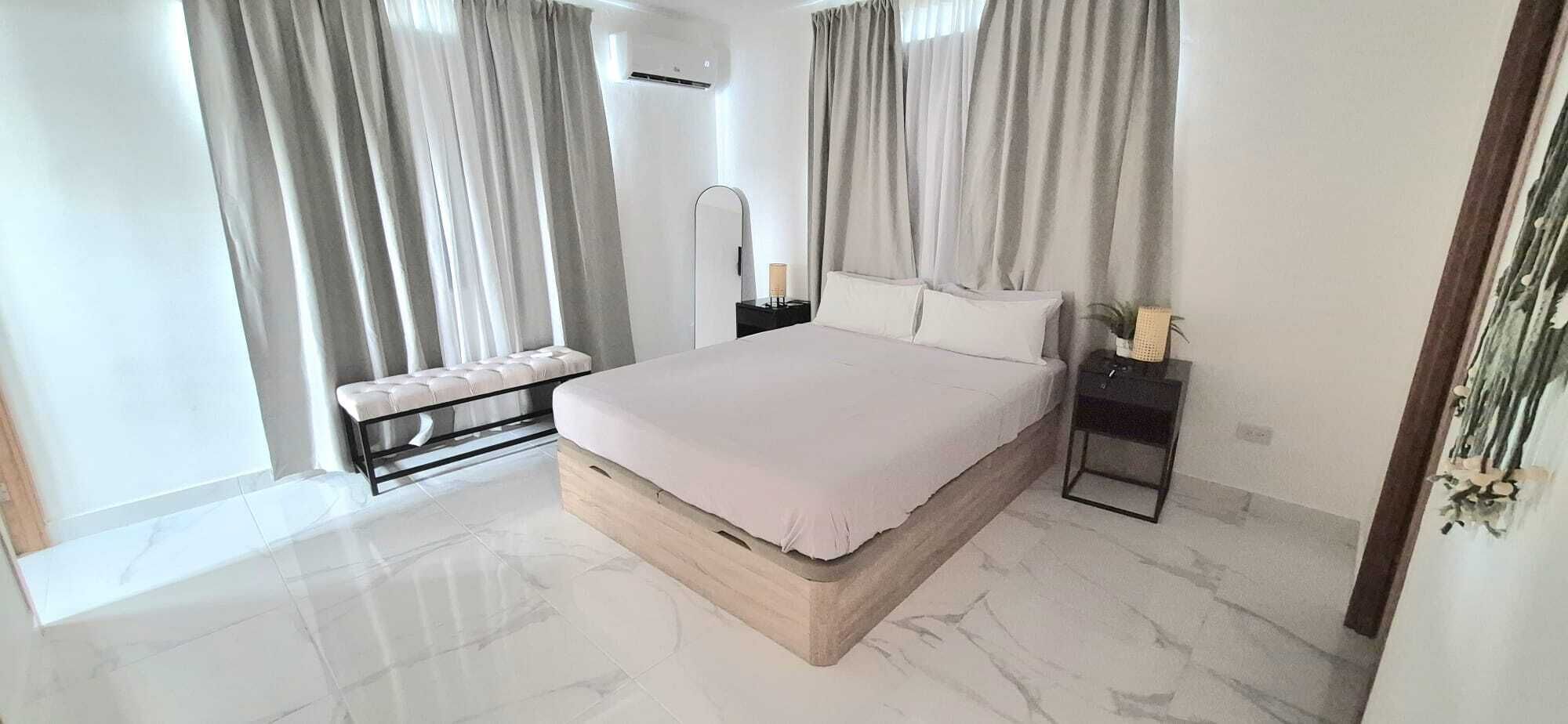 Ein modernes Schlafzimmer mit einem großen Bett, einer Bank, einem Nachttisch und einem Beistelltisch.