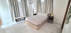 A modern bedroom with a large bed, a bench, a bedside table, and a nightstand.