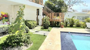 Une maison moderne dotée d’une piscine, d’un escalier en bois et d’un jardin où poussent différentes espèces de plantes.