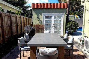 An outdoor patio with a table and chairs, a wooden fence, and a small shed with a door. - Charming 2 BR house with pool and hot tub walking distance to the beach/Las Olas (Fort Lauderdale)