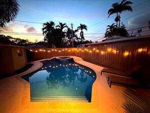 A swimming pool with a wooden deck and lounge chairs, surrounded by a wooden fence and palm trees. - Charming 2 BR house with pool and hot tub walking distance to the beach/Las Olas (Fort Lauderdale)