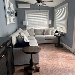 Una sala de estar con un sofá modular, una mesa redonda y un ventilador de techo.