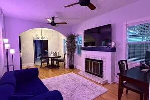 A living room with a fireplace, a ceiling fan, and a TV mounted above it. - Charming 2 BR house with pool and hot tub walking distance to the beach/Las Olas (Fort Lauderdale)