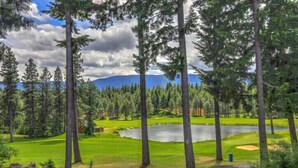 Un parcours de golf avec un lac, entouré de grands arbres et avec des montagnes en arrière-plan.
