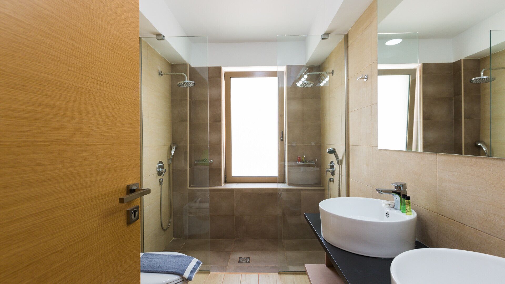 Une salle de bain moderne avec un grand miroir, deux lavabos, une douche et une fenêtre.