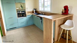 Une cuisine avec des meubles de couleur bleu clair, un plan de travail en bois, une machine à café rouge et une chaise blanche.