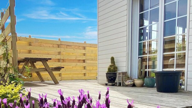 Une terrasse en bois avec une table et des chaises, une clôture en bois et des plantes en pot.