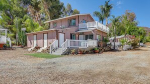 A two-story house with a balcony, surrounded by trees and a gravel driveway. - Lake Elsinore Apt 4 Mi to Water: Pets Welcome! (Lake Elsinore)