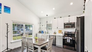 A modern kitchen with white cabinets, stainless steel appliances, and a dining area with a wooden table and chairs.