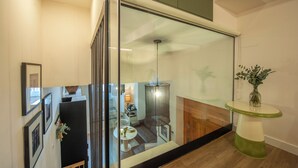 Interior moderno com divisória de vidro, área de refeições com mesa e cadeiras, luminária pendente e pequena mesa com um vaso.