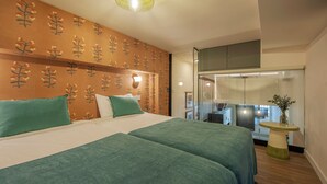 Quarto de hotel com uma cama grande, duas almofadas, uma mesa pequena com um vaso e vista da cidade através de uma porta de vidro.