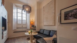 Uma sala de estar moderna com um sofá de couro preto, uma mesa de centro redonda, uma luminária pendente e uma janela grande com persianas.
