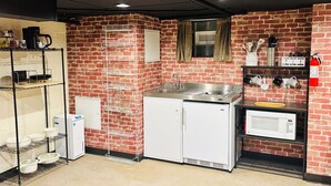 Eine kleine Küche mit Backsteinwand, weißen Schränken, einer Edelstahl-Spüle, einer Mikrowelle und einer Kaffeemaschine.