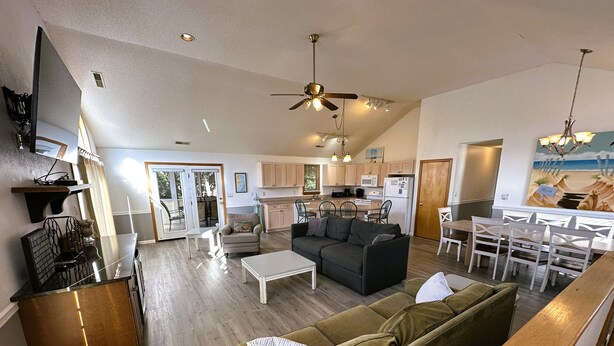 A spacious living area with a sofa, coffee table, and dining table. There is a kitchen in the background with cabinets and appliances.