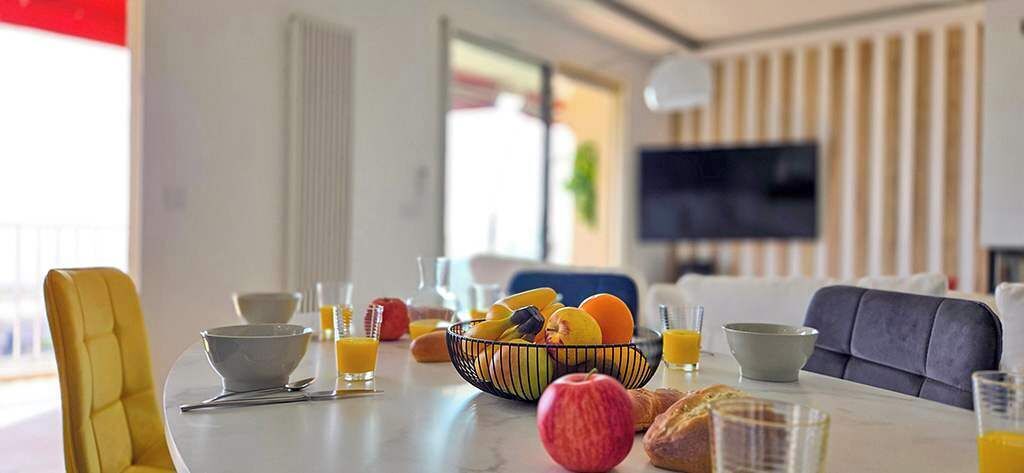 A dining table with fruits, glasses, and a bowl of oranges.
