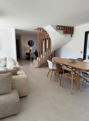 A modern living space with a sofa, dining table, chairs, and a staircase.