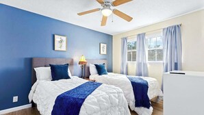Una habitación con dos camas, un ventilador de techo y una ventana con cortinas.