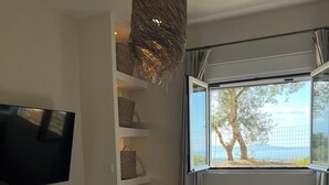 A modern bedroom with a bed, a television mounted on the wall, and a window with a view of trees and a fence. - Earthouse Rethymno (Rethimno)