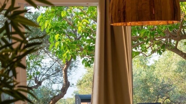 A modern interior with a large window, a hanging wooden pendant light, and a view of the outdoors. - Earthouse Rethymno (Rethimno)