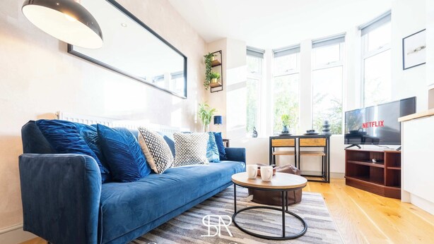 Uma sala de estar com um sofá azul, uma mesa de centro e uma televisão exibindo 'NETFLIX'.
