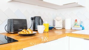 Uma cozinha moderna com cafeteira, chaleira, torradeira, um prato de croissants, um copo de suco de laranja e um tablet no balcão.