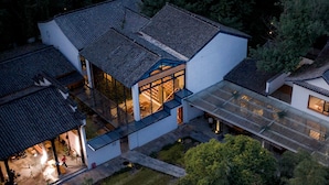 An aerial view of a modern house with a large glass facade, surrounded by dense trees. - Wangshanlife Snow Garden Design Hotel (Huangshan)