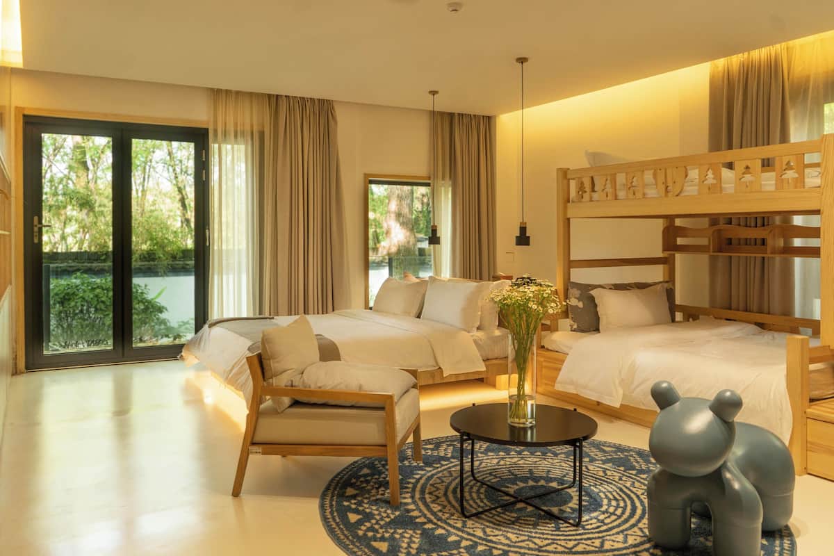 A hotel room with a large bed, a smaller bed, a sofa, a coffee table, and a view of greenery outside.