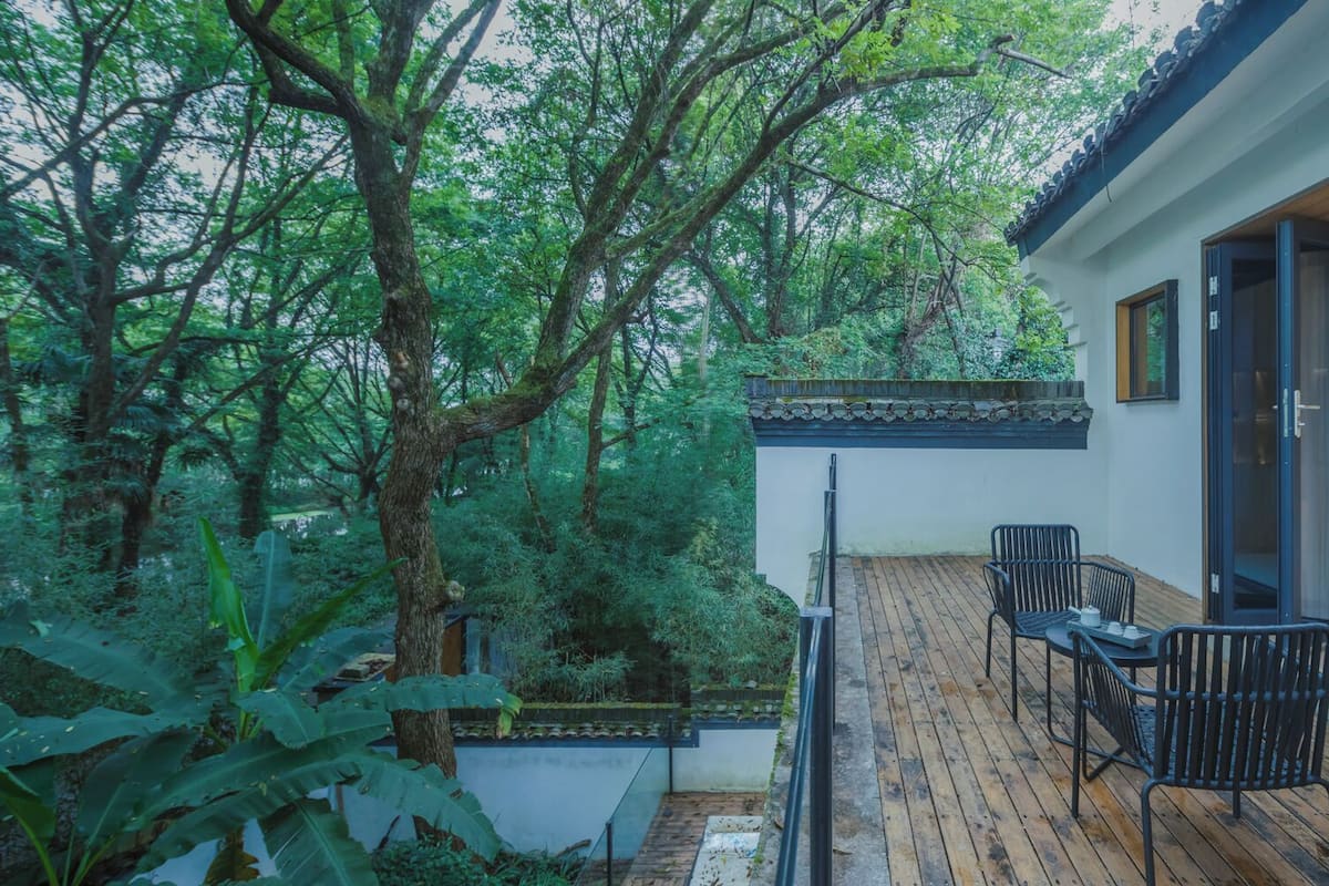 A modern outdoor deck with a wooden floor, surrounded by lush greenery and trees.