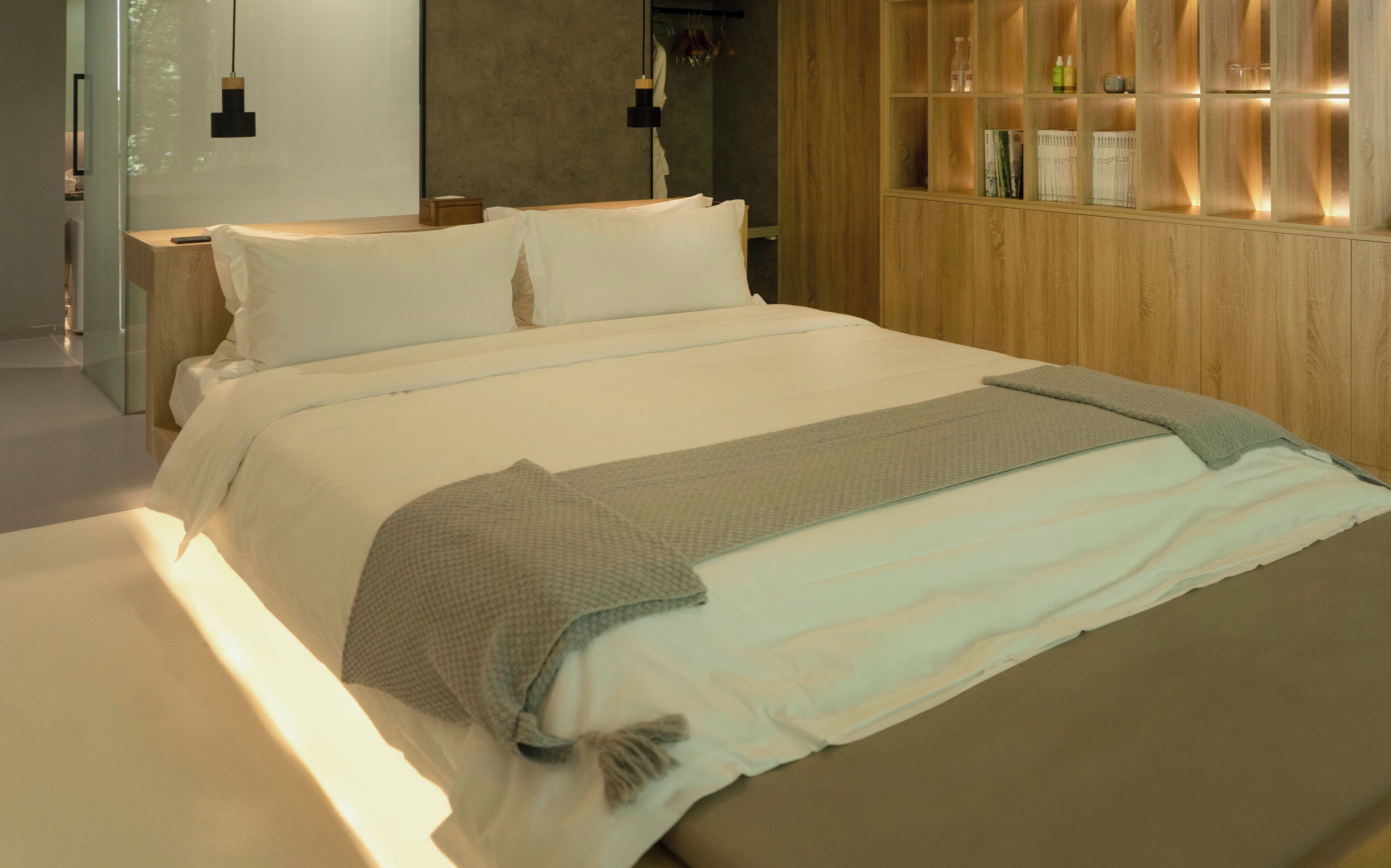 Een moderne slaapkamer met een groot bed, nachtkastjes, een houten garderobe en een hanglamp.