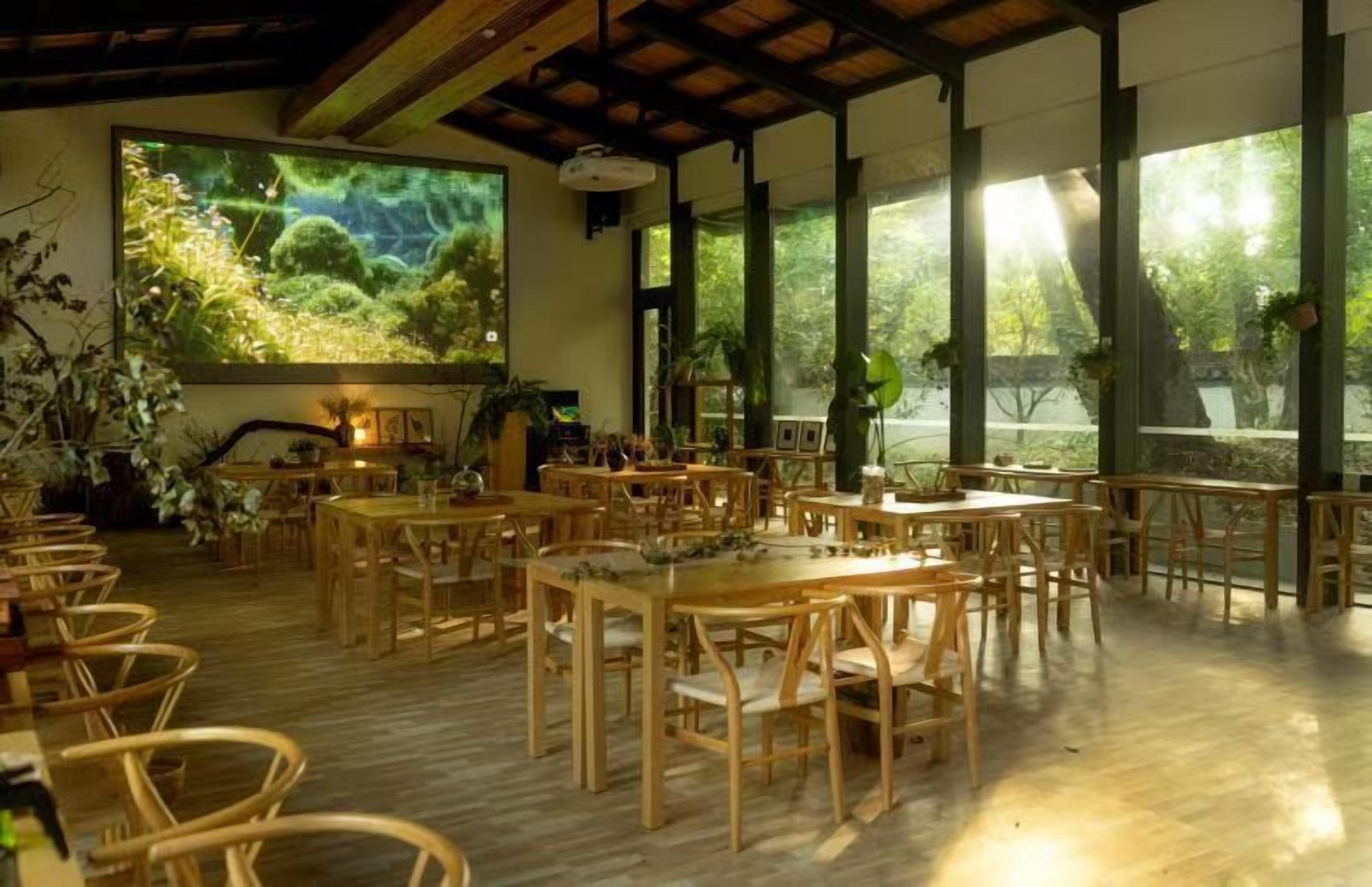 A spacious room with wooden tables and chairs, large windows with natural light, and a large screen displaying a nature scene.