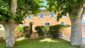 Ein gepflegter Garten mit Rasen, Bäumen und einem Gebäude mit vielen Fenstern und Fensterläden.