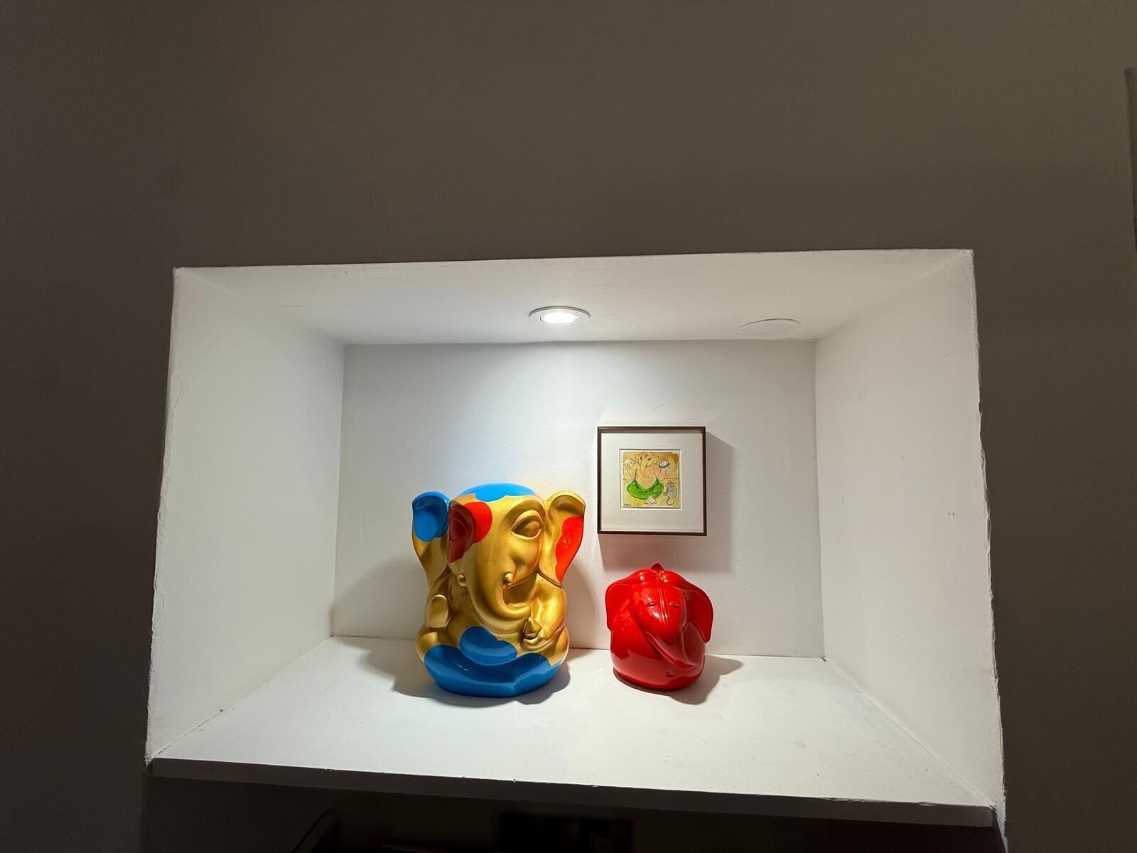 Une étagère blanche ornée de deux sculptures colorées et d’un tableau encadré.