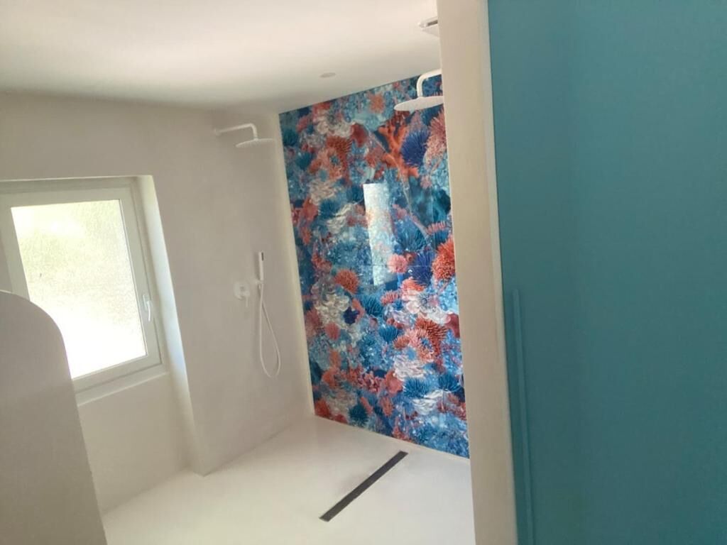 A small, bright room with a window, a shower, and a colorful wall mural.