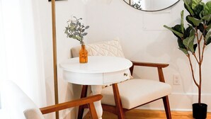 Una habitación con una mesa redonda blanca, una silla de madera, una planta en maceta y un espejo en la pared.