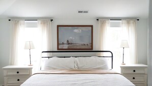 Un dormitorio ordenado con una cama, dos mesitas de noche y un cuadro sobre la cama.