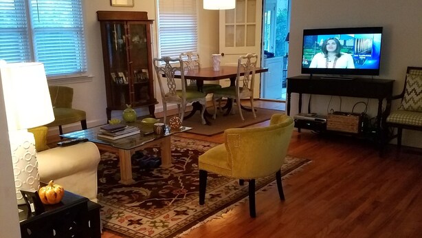 A living room with a wooden floor, a dining table with chairs, a television, and a ceiling fan. - Cozy cottage home just one mile from Augusta National. (Augusta)