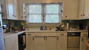 A kitchen with white cabinets, a stove, a sink, and a window with blinds. - Cozy cottage home just one mile from Augusta National. (Augusta)