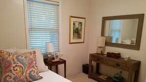 A bedroom with a bed, a bedside table with a lamp, a dresser, a mirror, and a window with blinds. - Cozy cottage home just one mile from Augusta National. (Augusta)
