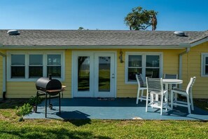 Ein gelbes Haus mit überdachter Terrasse, Grill und Esstisch mit Stühlen.