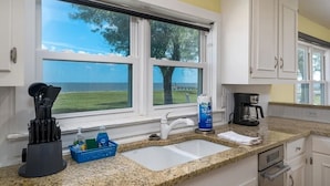 A kitchen with a large window, granite countertop, white cabinets, and a coffee maker. - Island Time 3 Bedroom Home (Rockport)