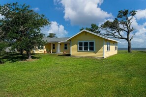 Ein gelbes Einfamilienhaus mit Veranda, umgeben von einem gepflegten Rasen und Bäumen.