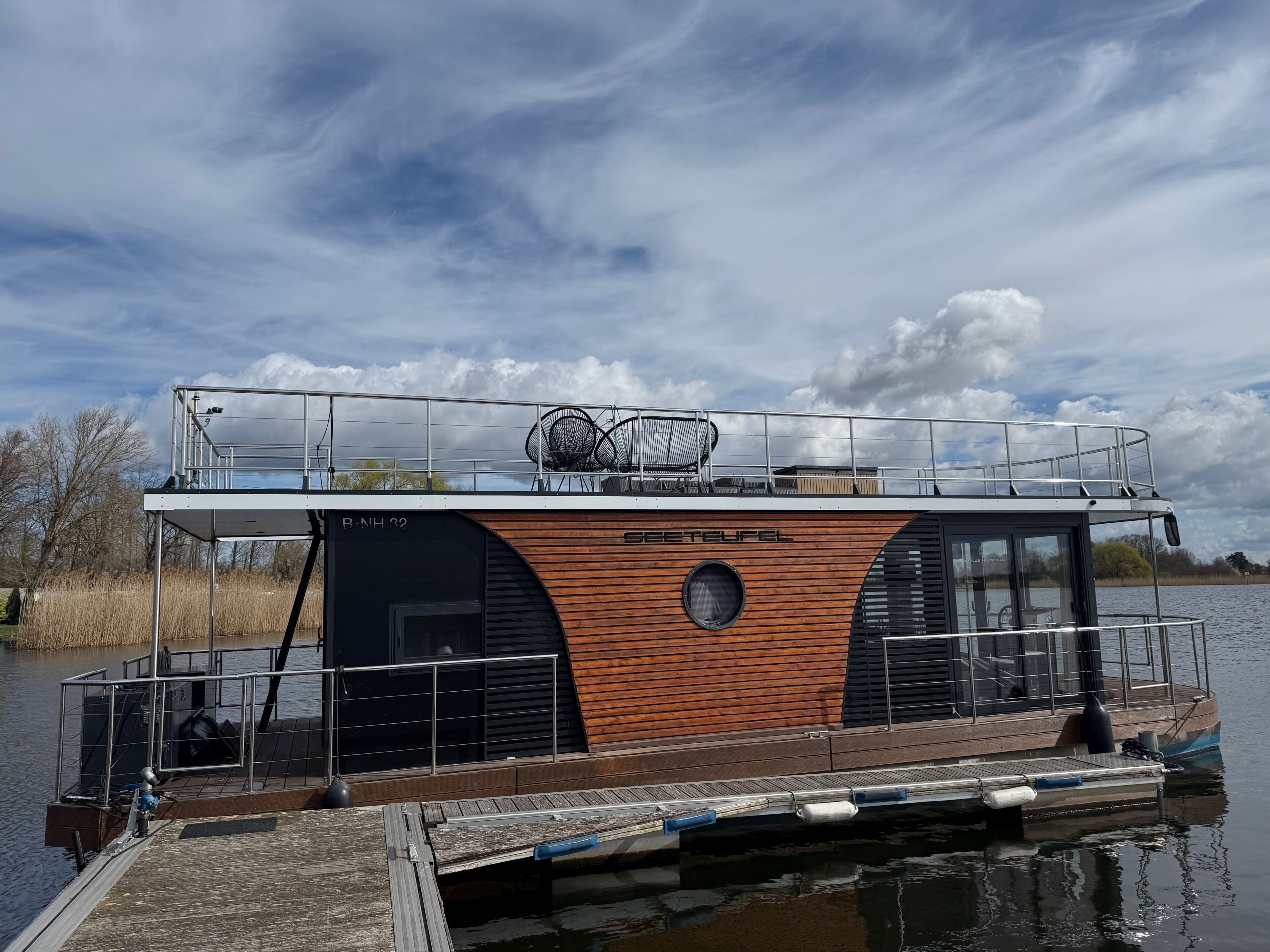 Una casa flotante con terraza, una zona cubierta con asientos y un ventanal grande.