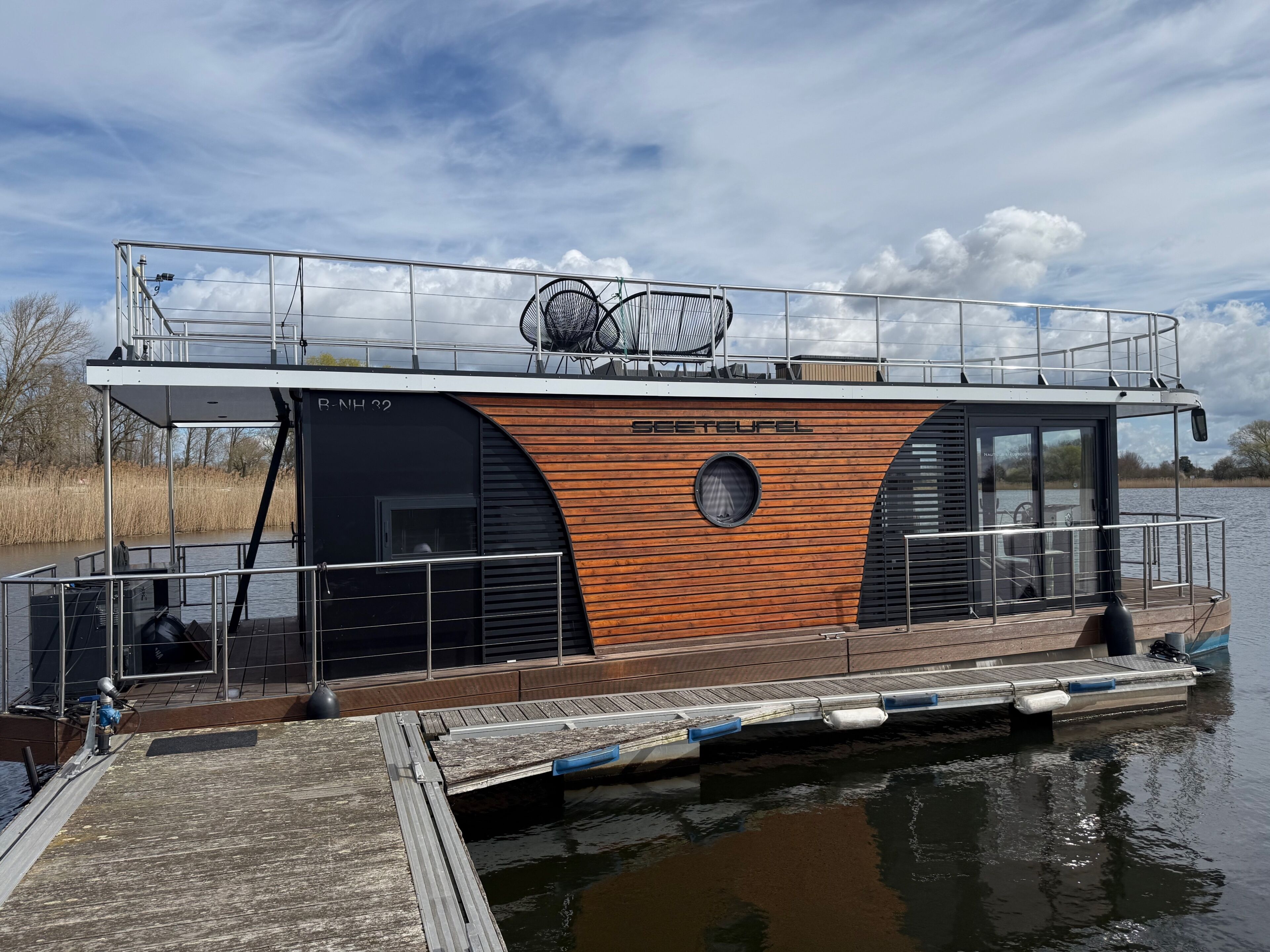 Ein Hausboot mit Deck, einem überdachten Bereich und dem Schriftzug 'SEETEUFEL' an der Seite.