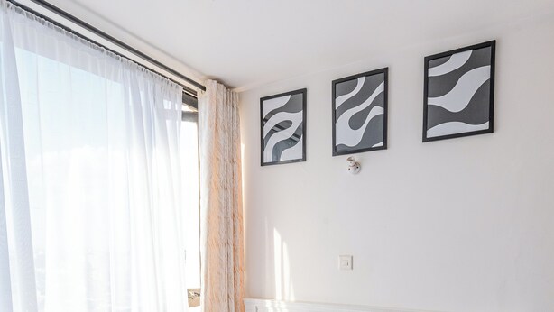 A neatly made bed with white linens and a single orange pillow, a white headboard, and three abstract wall art pieces.