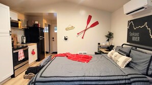 Un dormitorio moderno con una cama grande, kitchenette y aire acondicionado de pared.