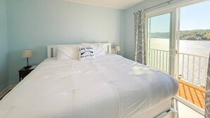 Un dormitorio con cama, ventilador de techo, mesita de noche y ventana con vistas a un lago.