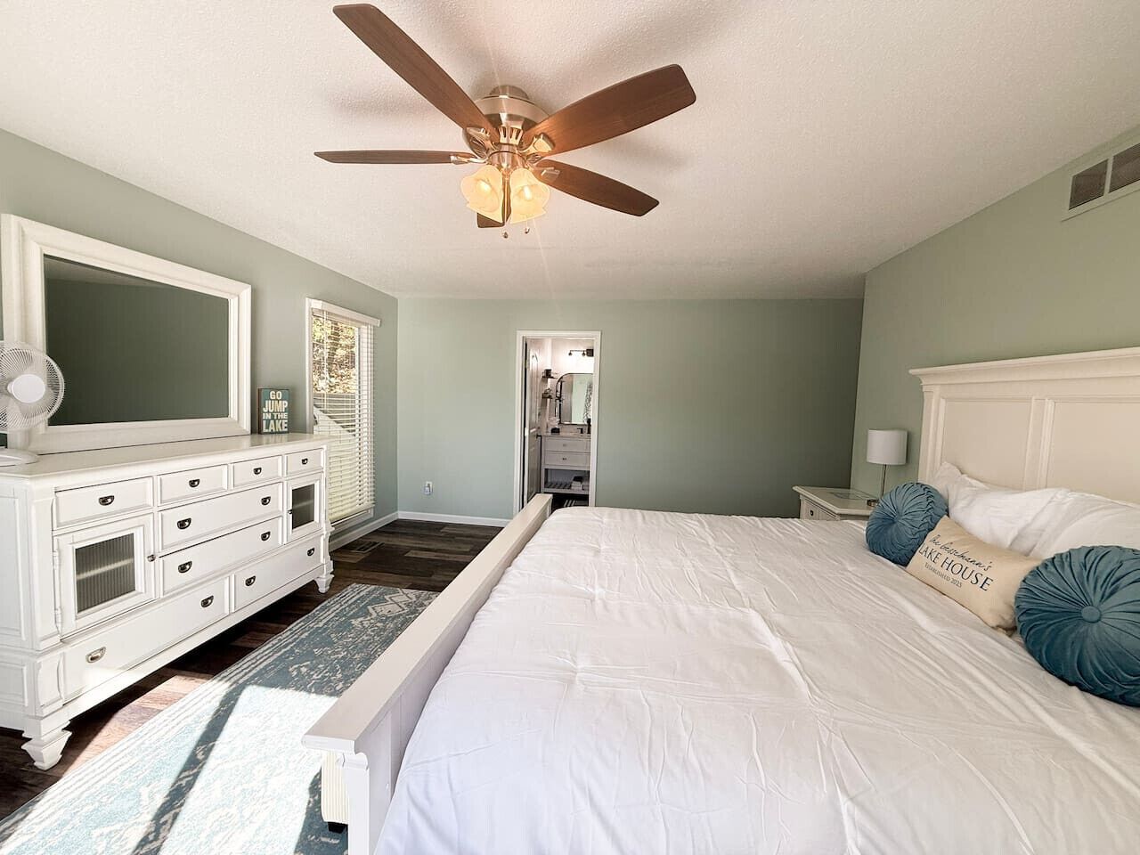 A bedroom with a bed, dresser, ceiling fan, and a view into another room.