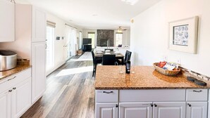 Una cocina moderna con armarios blancos, encimera de granito y un comedor con mesa y sillas.
