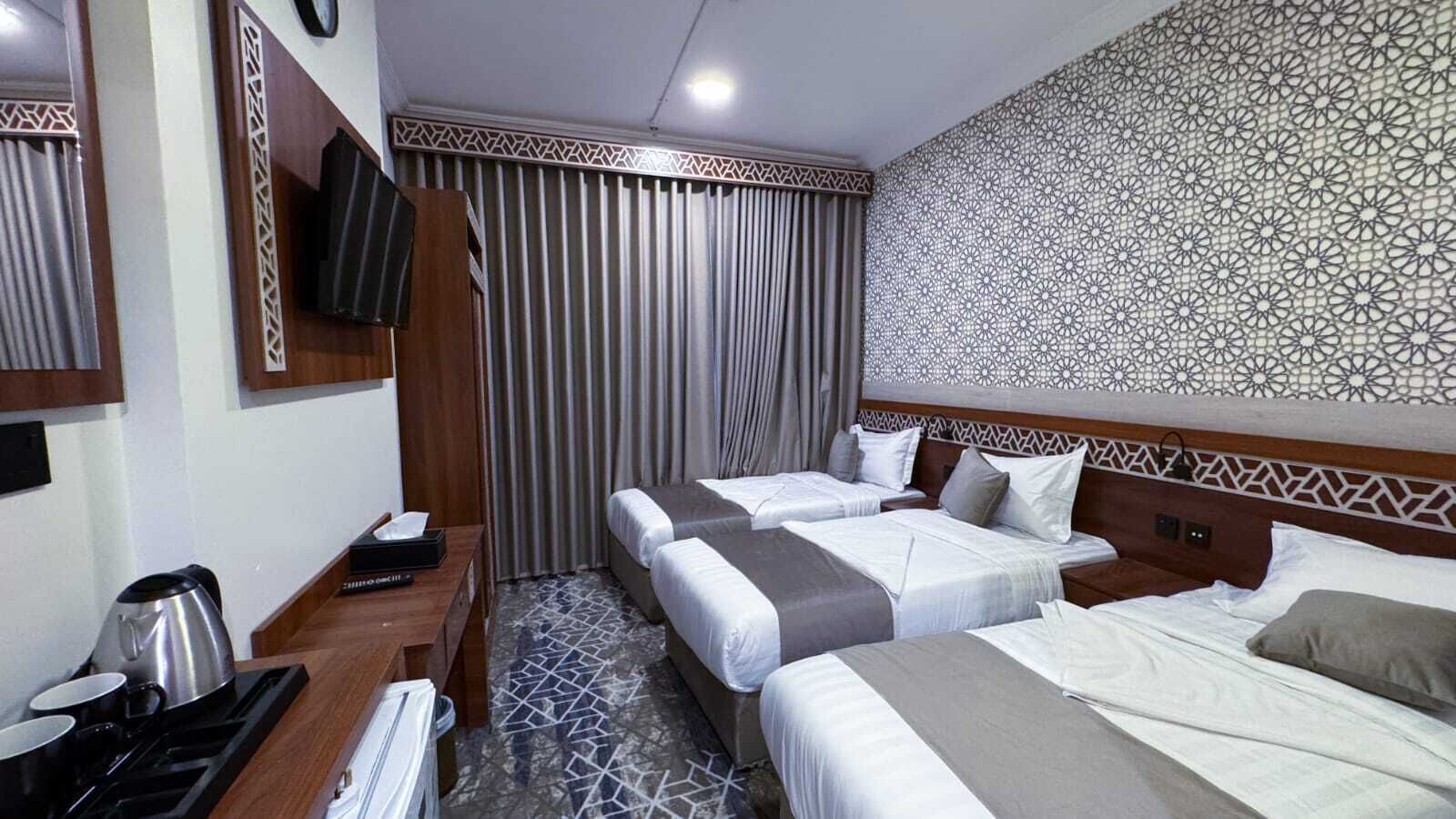 Quarto de hotel com duas camas, uma escrivaninha com chaleira e parede estampada.